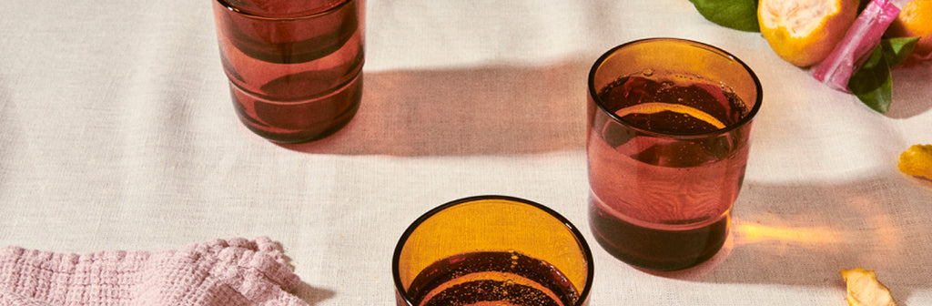 Two glasses of pink lemonade on a light wooden surface with a pink cloth and lemon slices.