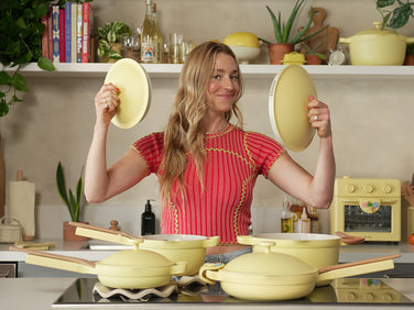 Woman in a kitchen holding yellow kitchen items with a shelf of books and decor in the background
