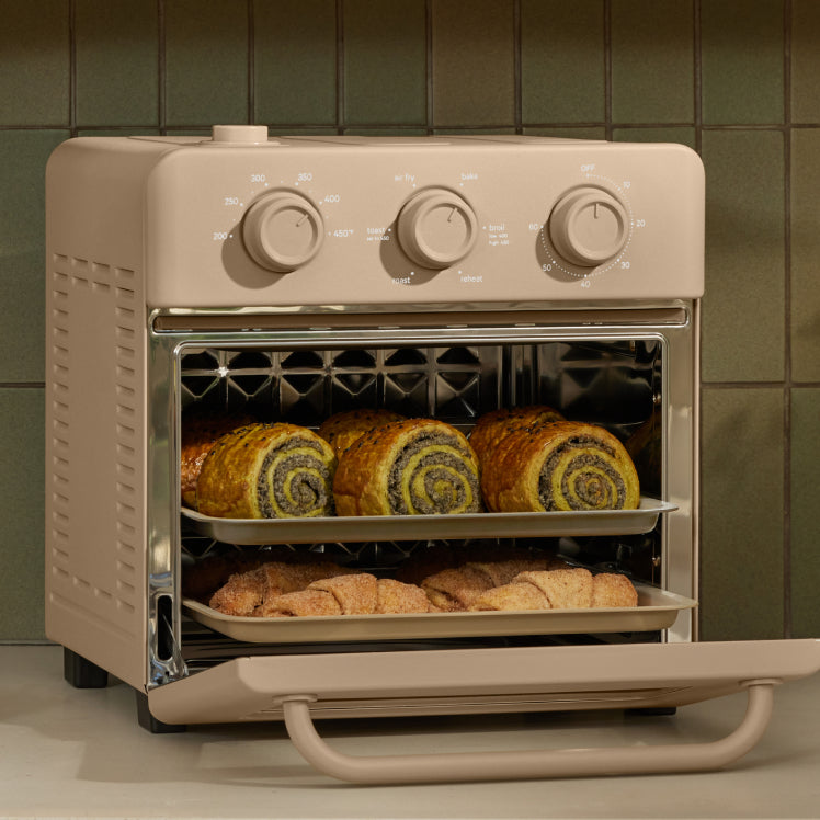 Beige toaster oven with baked goods on a green tiled wall background