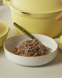 Bowl of pasta with a fork, yellow pot in the background