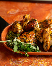 Roasted chicken pieces garnished with fresh sage, thyme, and parsley on an oval terracotta platter.