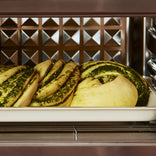 Pesto-swirled dough rolls on a baking sheet inside an oven.