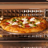 A pizza topped with dollops of white cheese, sliced zucchini, tomatoes, and herbs inside an oven.
