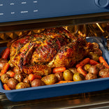 A roasted chicken surrounded by potatoes and carrots in a baking pan inside an air fryer oven.
