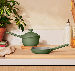 Green cookware set on a wooden surface with a plant in the background