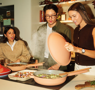 Three people cooking together in a kitchen with steam rising from pans.