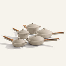 The Cookware Set+ includes five beige nonstick pots and pans with matching lids and wooden handles, displayed on a light background.