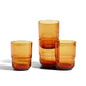 Three amber-colored glass tumblers of varying heights are placed together on a white background.