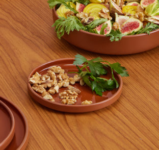 A small terracotta plate with walnuts and parsley sits next to a larger bowl containing a salad with figs, yellow beets, greens, and walnuts on a wooden table.