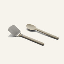 A Titanium Pro Utensil Set featuring a metal spatula and a solid-colored spoon side by side.