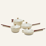 The Cookware Set includes four cream pots and pans with brown handles and gold knobs, inspired by the Always Pan and Perfect Pot, shown on a neutral background.