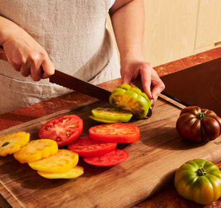 Person slicing tomatoes on a wooden cutting board.