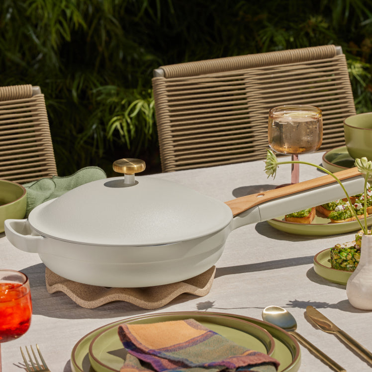 A white Always Pan rests on a Pleat Trivet atop a table set with green dinnerware